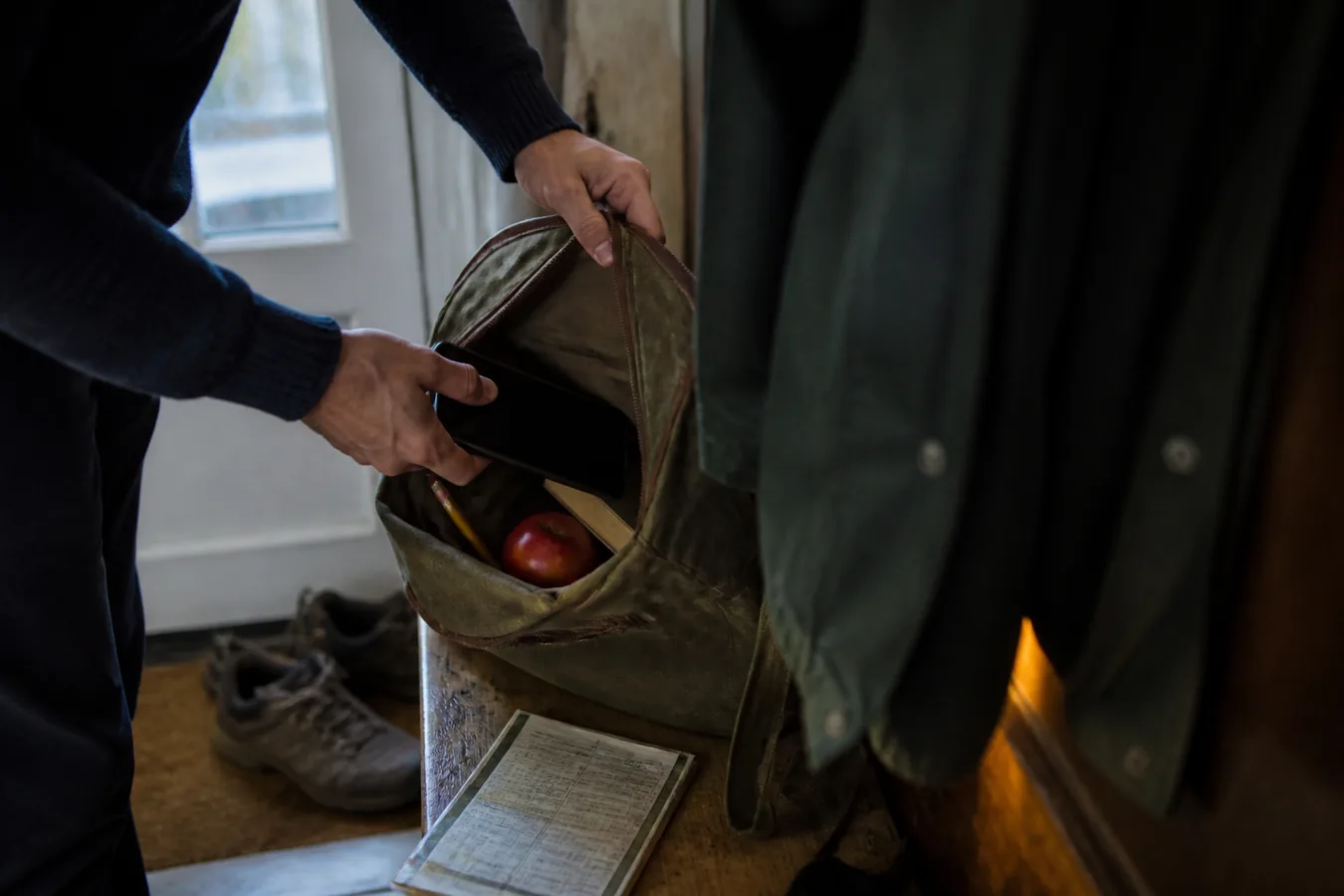 A person putting a powered-off phone into a worn canvas bag