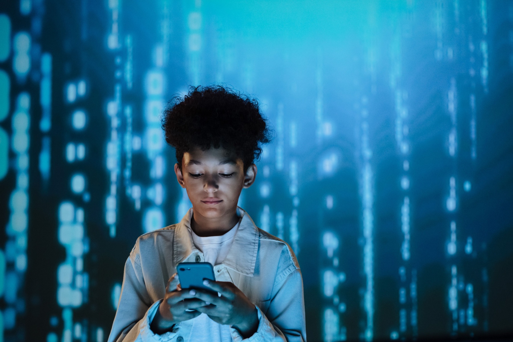 A child looking down at a phone in blue light