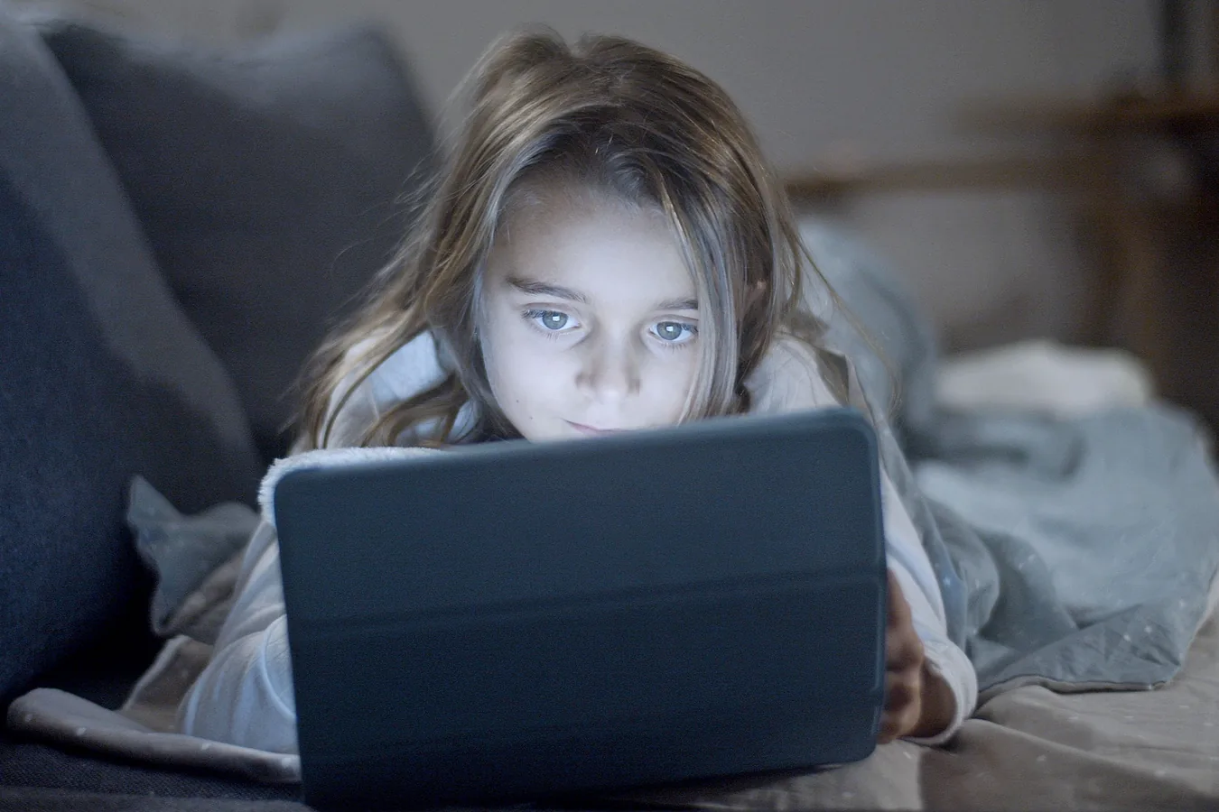 A child looking closely at a tablet in a dim room