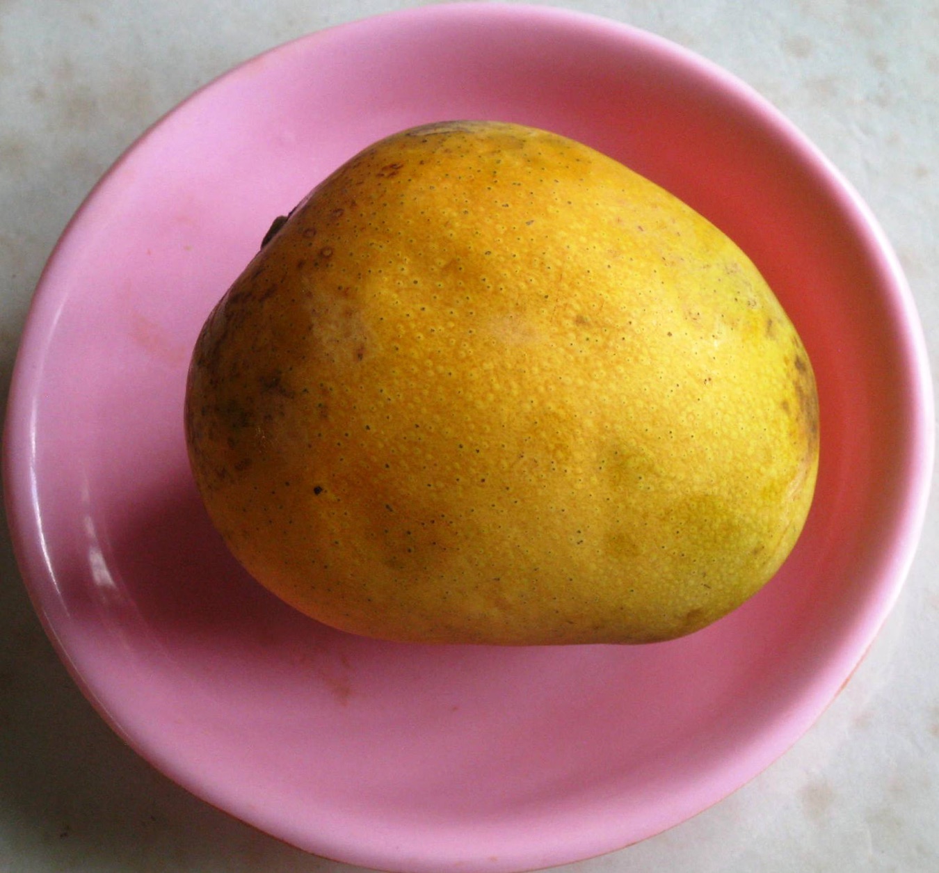 A yellow Himsagar mango on a pink plate