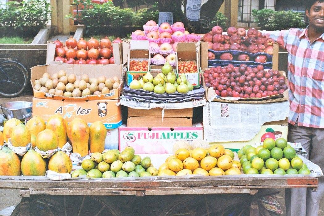 A smiling fruit seller beside a cart of mangoes, pears, apples and other fruit