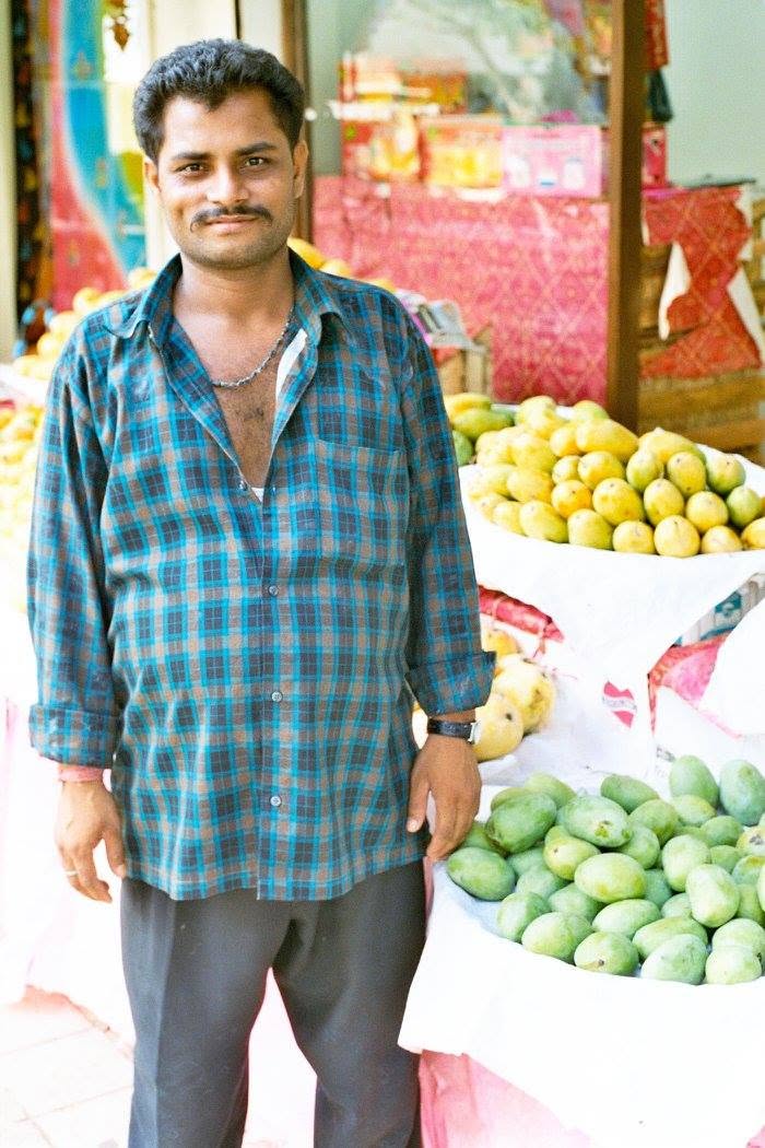 A mango seller standing in front of several piles of green and yellow mangoes