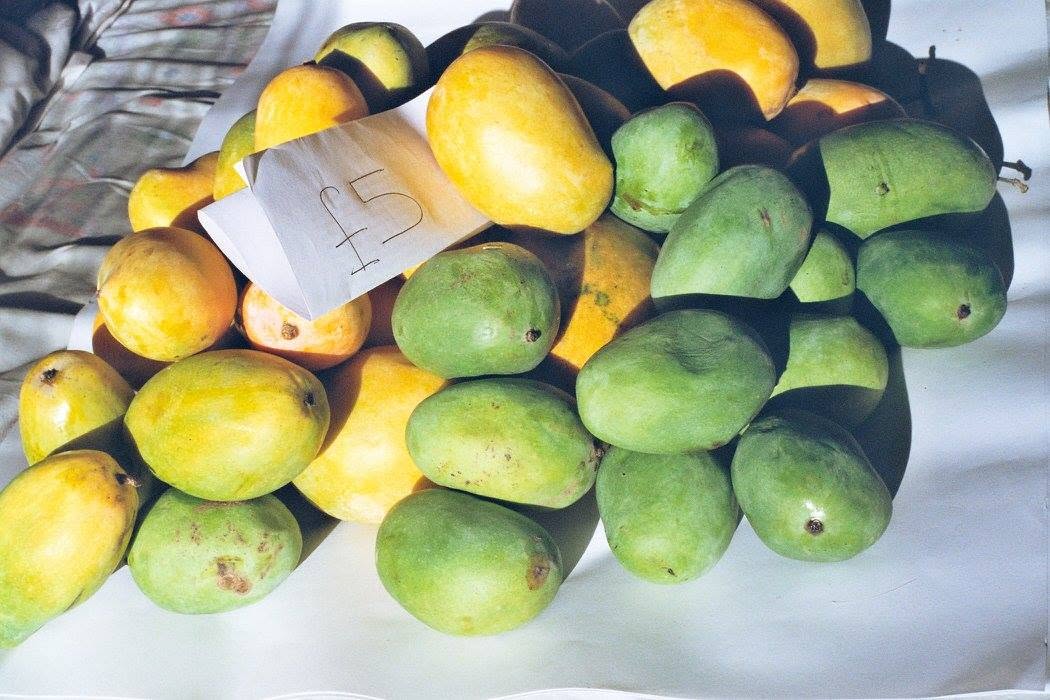 A pile of green and golden mangoes marked with a handwritten five-pound price