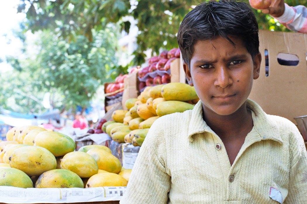 A young mango seller standing beside boxes and piles of yellow-green mangoes