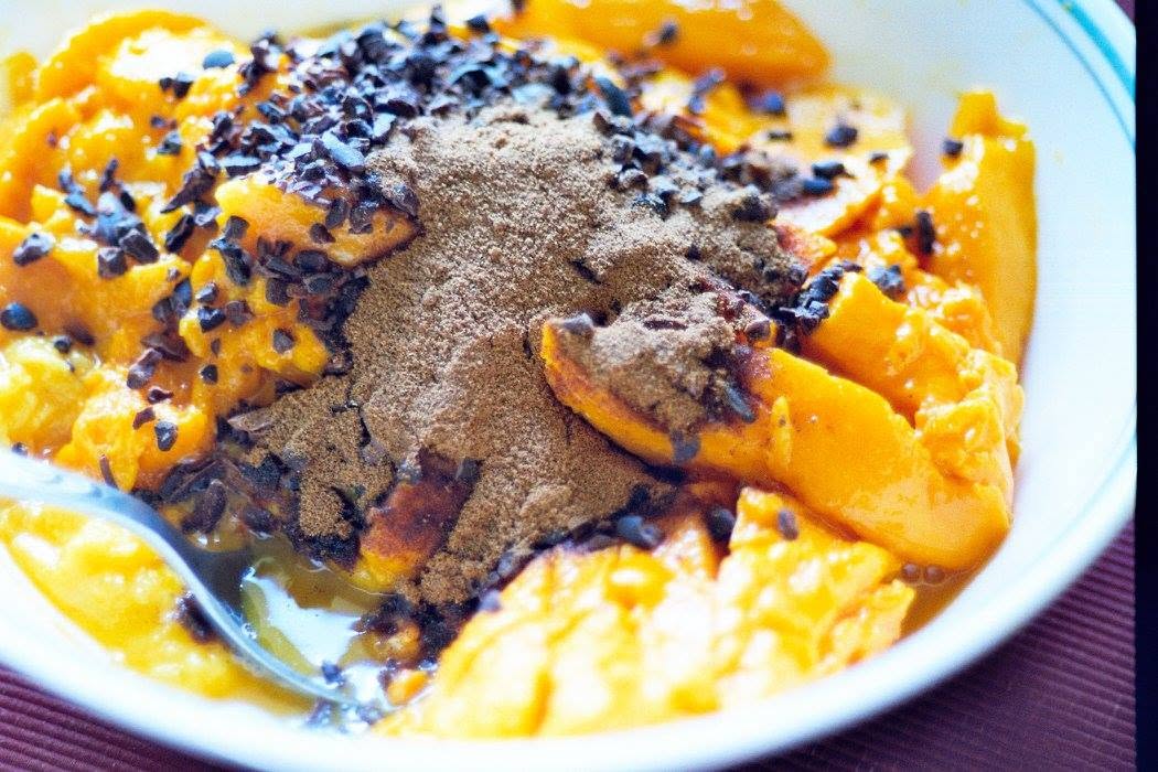 Cut mango topped with cacao nibs and carob powder in a bowl