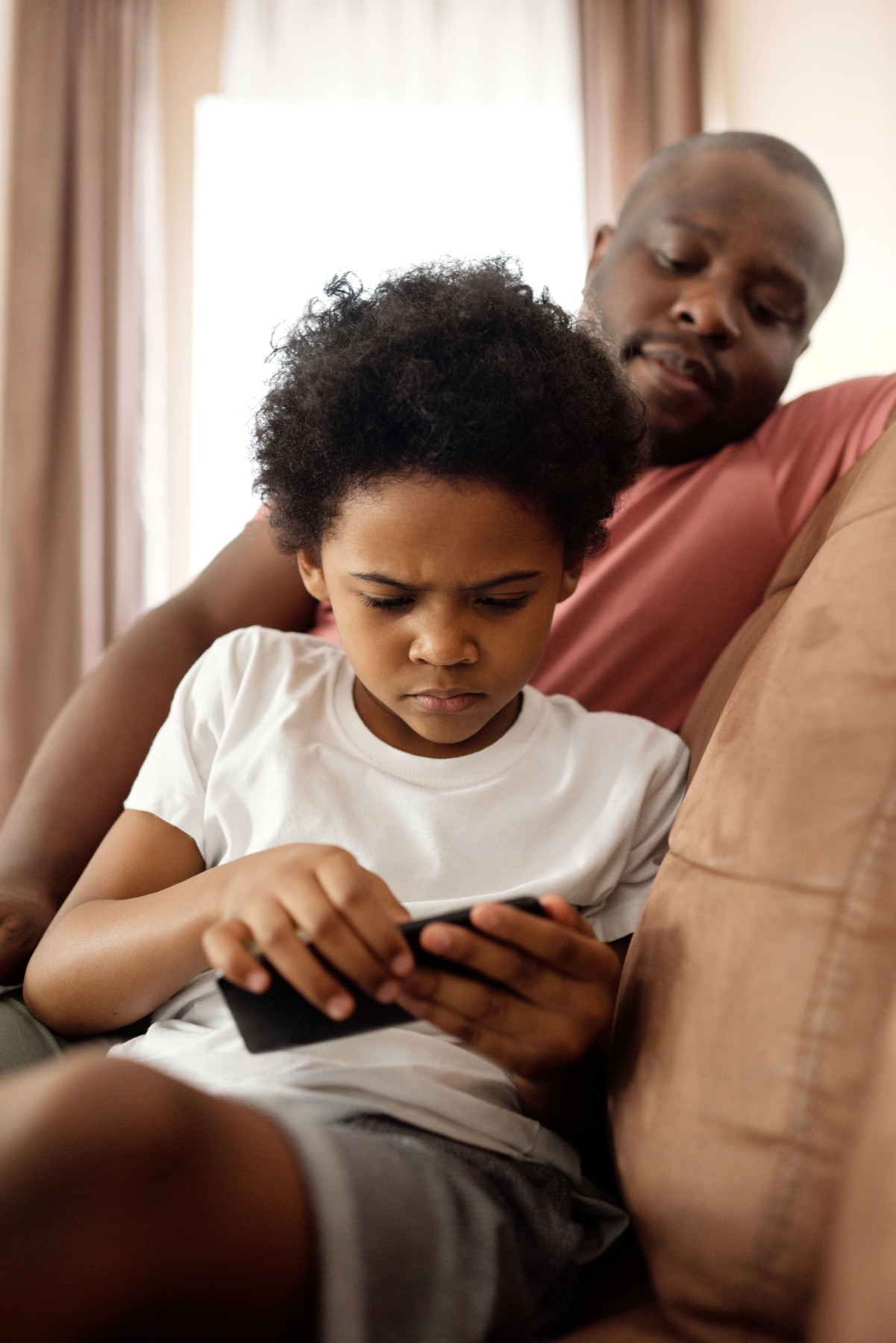 A father sitting with his child while the child uses a phone
