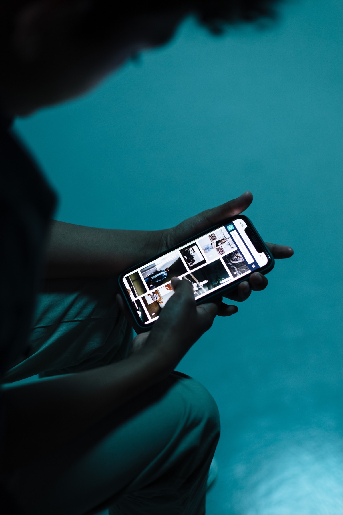 A person scrolling through photographs on a phone in blue light