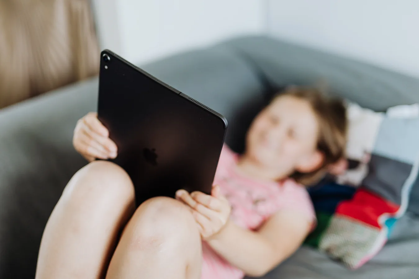 A child relaxing on a sofa while holding a tablet