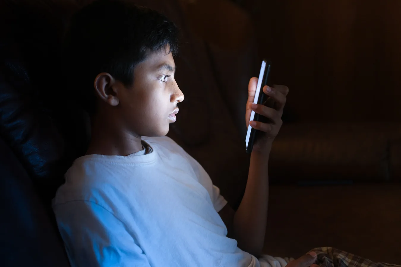 A teenage boy looking at a phone in a dark room
