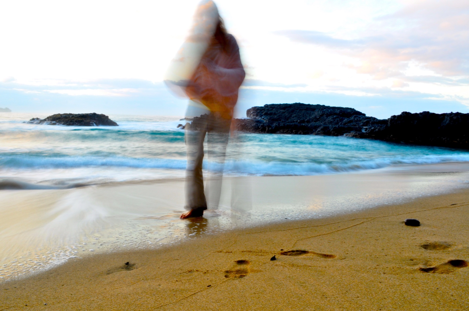 A long-exposure photograph of Michael Mackintosh walking beside the sea