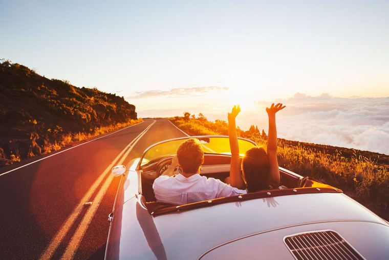 Two people driving beside the ocean with the roof down